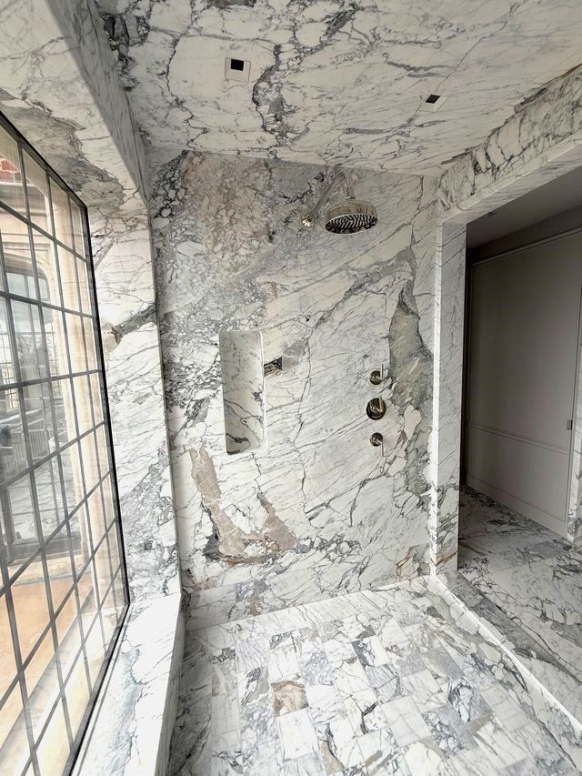 A bathroom with marble walls and a shower head.