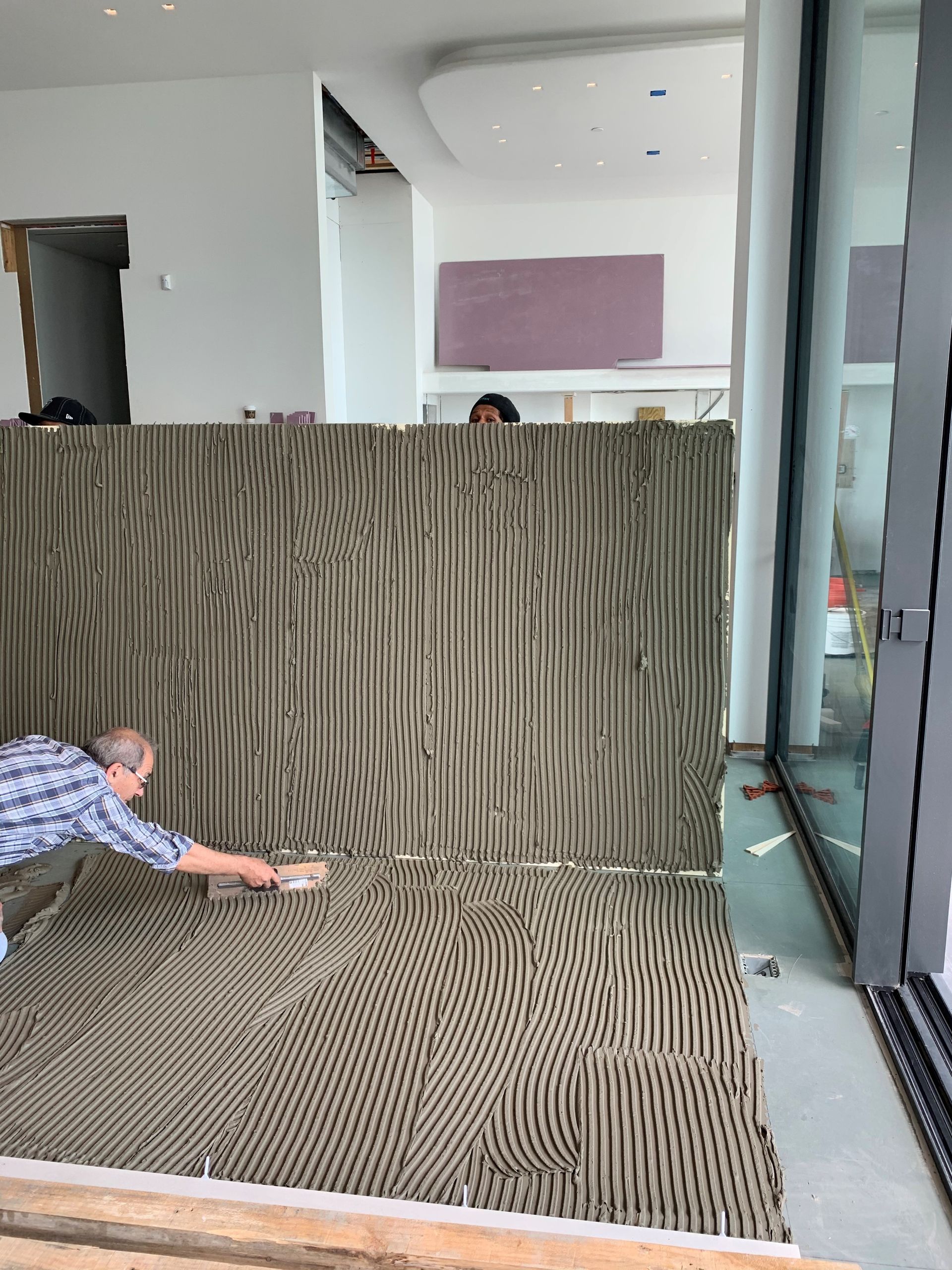 A man is laying tile on the floor in a room.