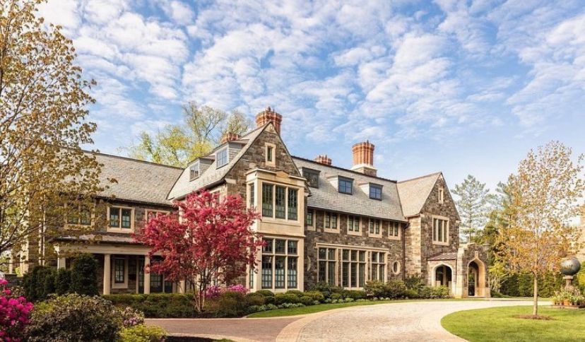 A large house with a driveway leading to it is surrounded by trees and bushes.