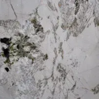 A close up of a white marble counter top with green and black spots.