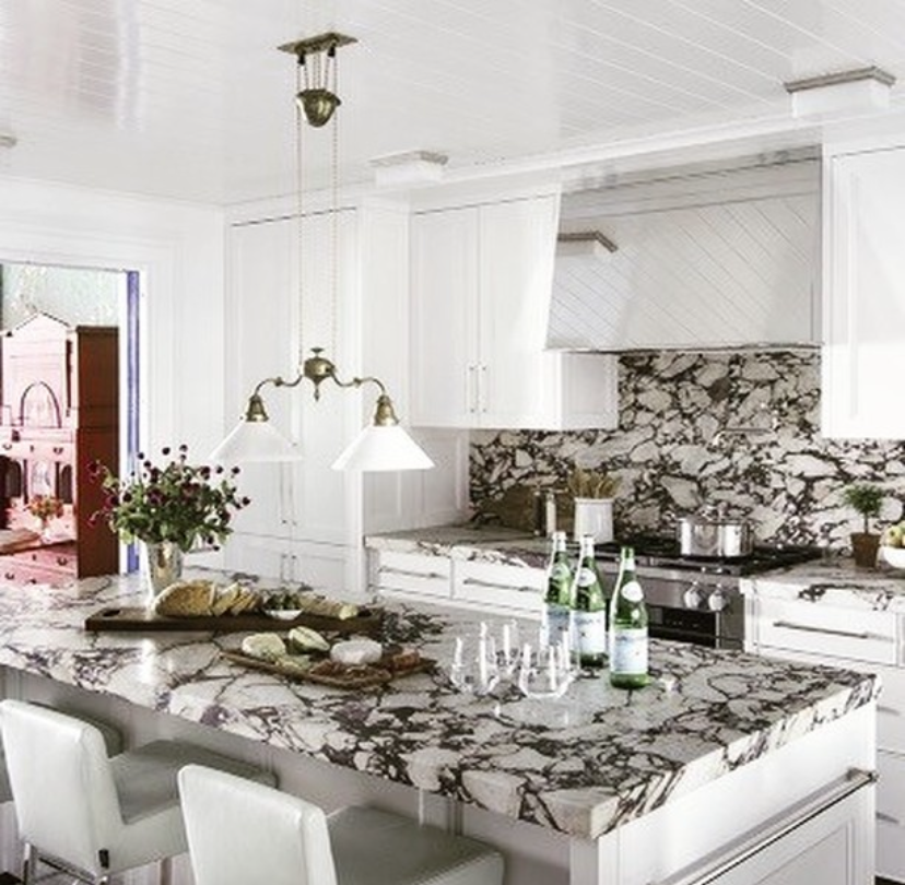 A kitchen with a marble counter top and white cabinets