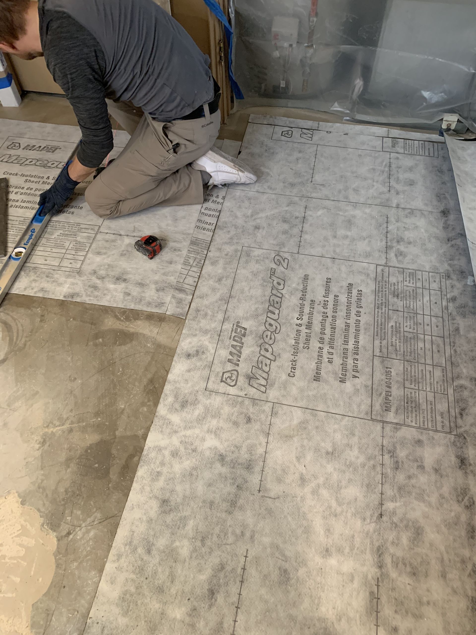 A man is kneeling on the floor with a measuring tape.