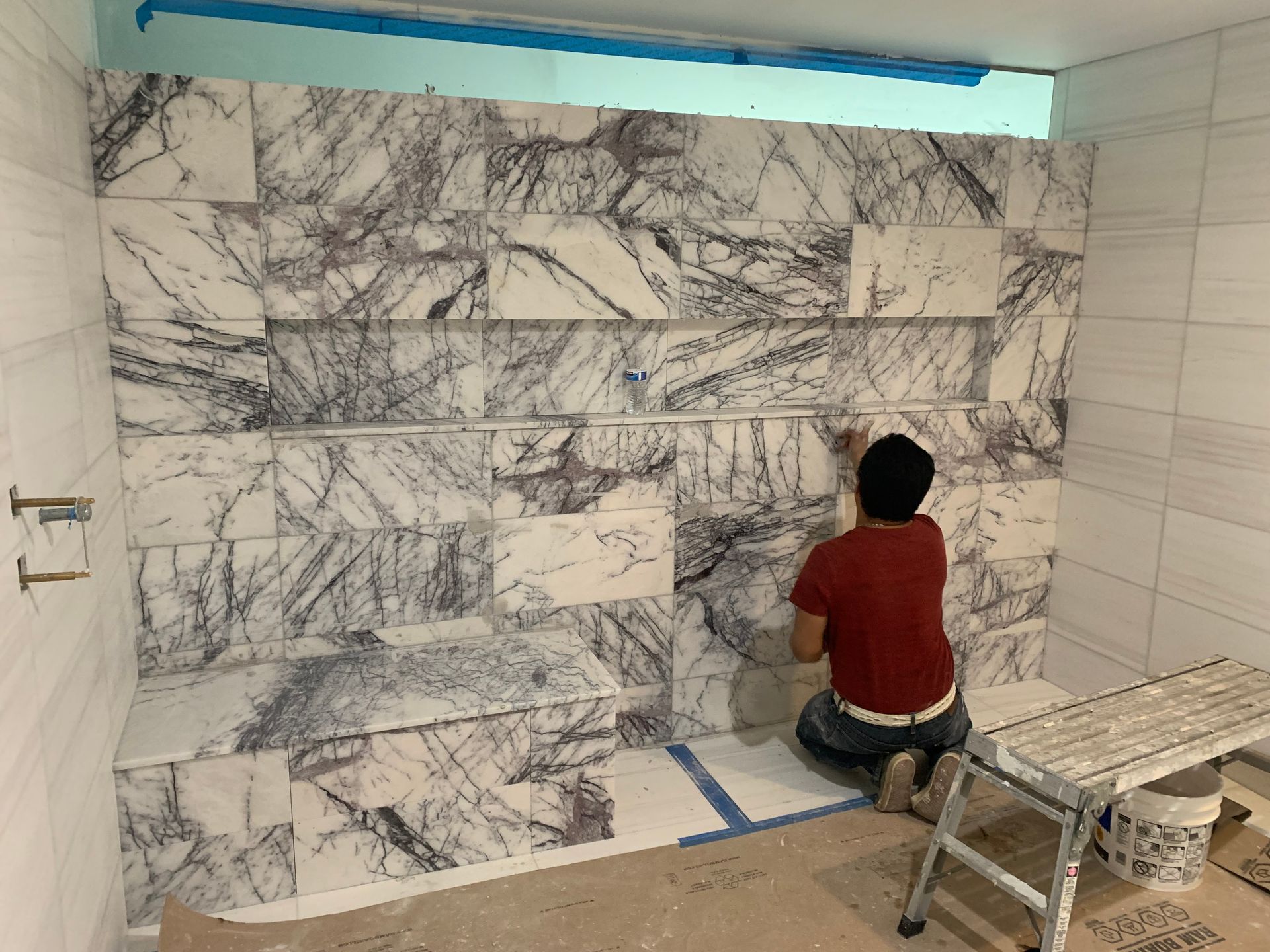 A man is kneeling down in front of a marble wall.