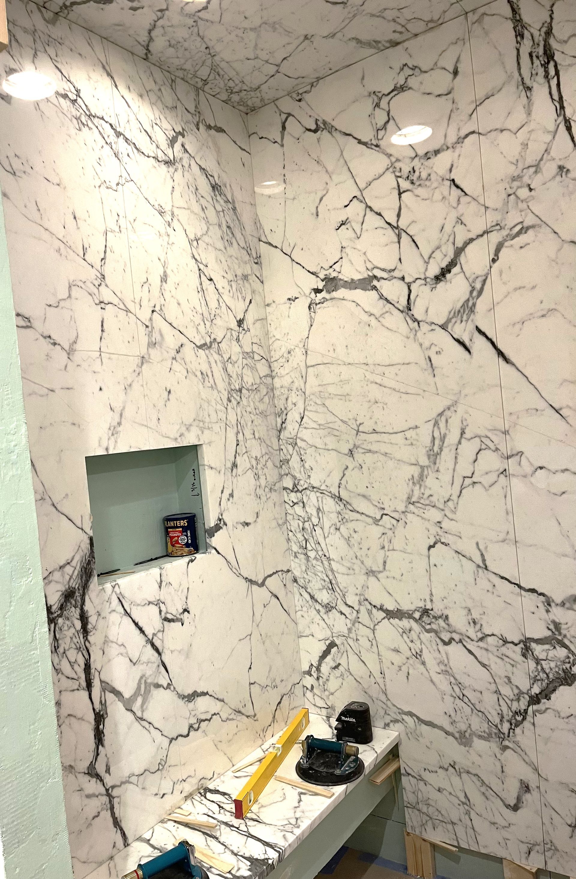 A bathroom with a marble wall and a shelf in the shower.