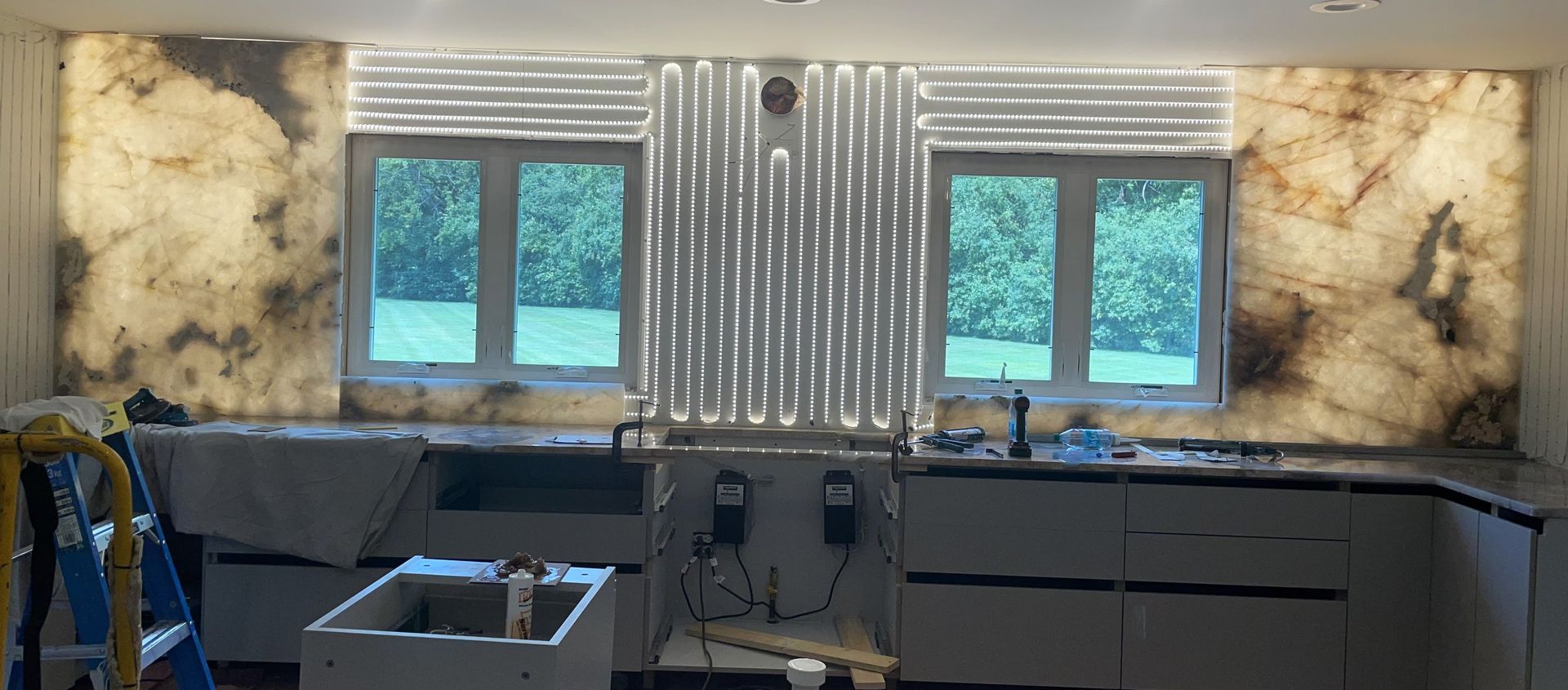 A kitchen with a sink , cabinets , and a large window.