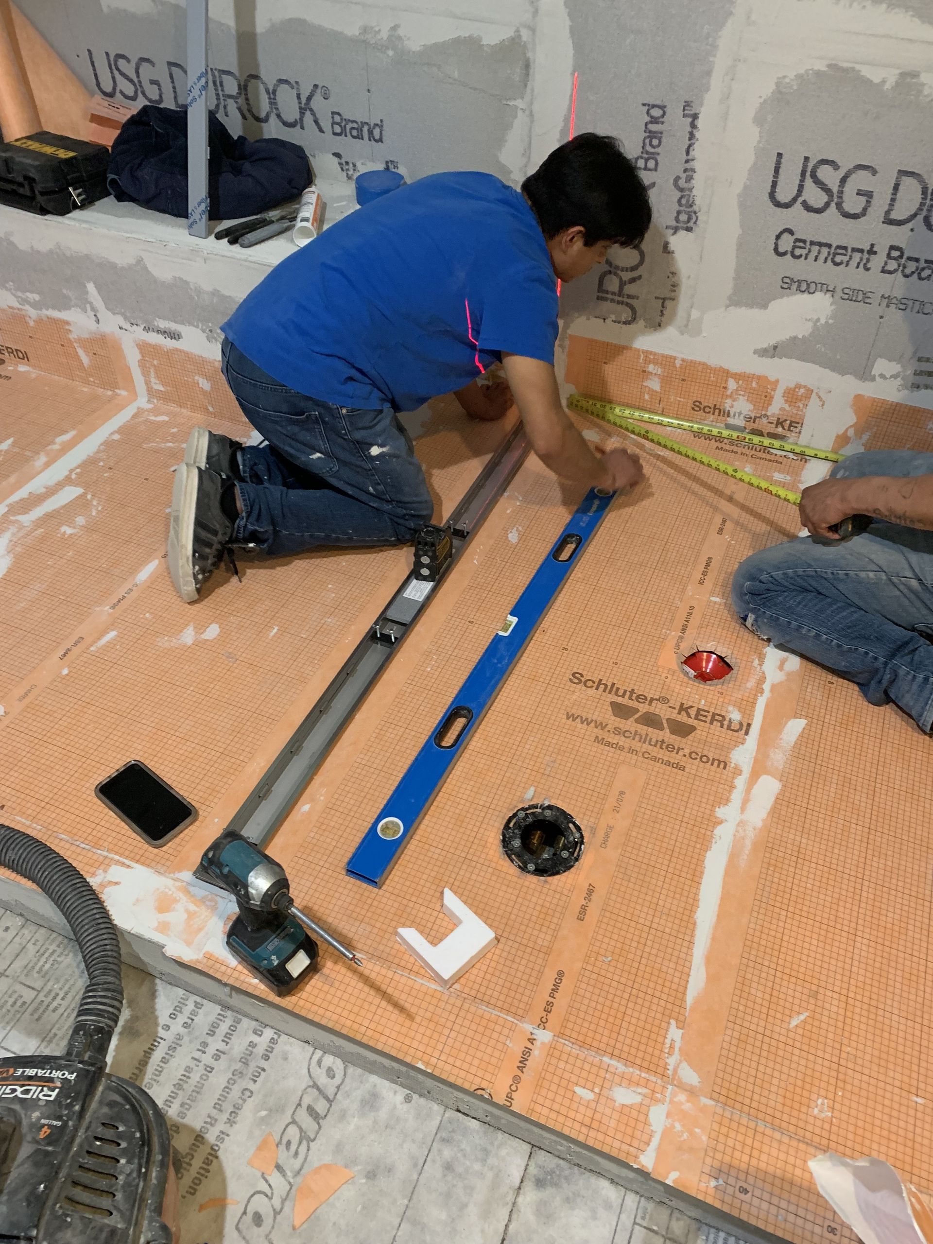 A man is kneeling on the floor measuring something with a level.