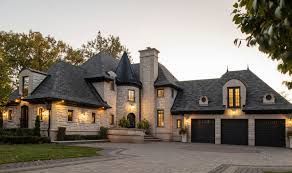 A large house with three garages and a castle roof is sitting on top of a lush green hillside.