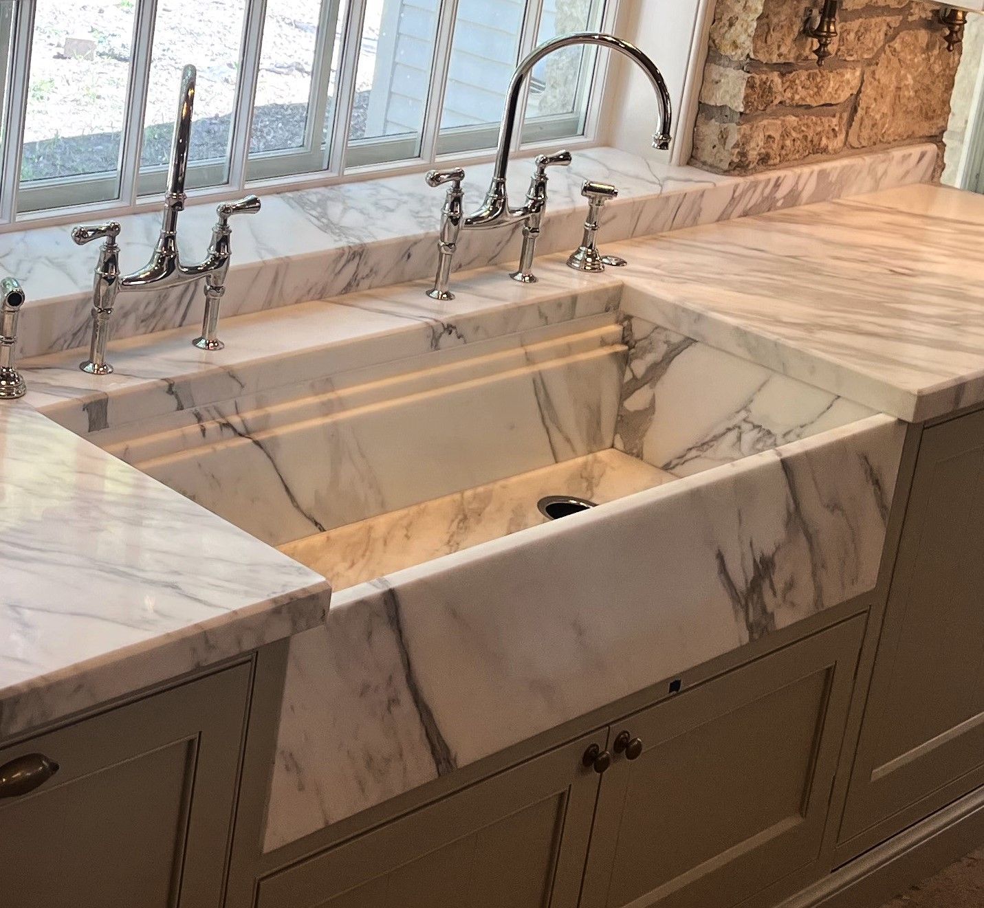 A kitchen sink with a marble counter top and a window