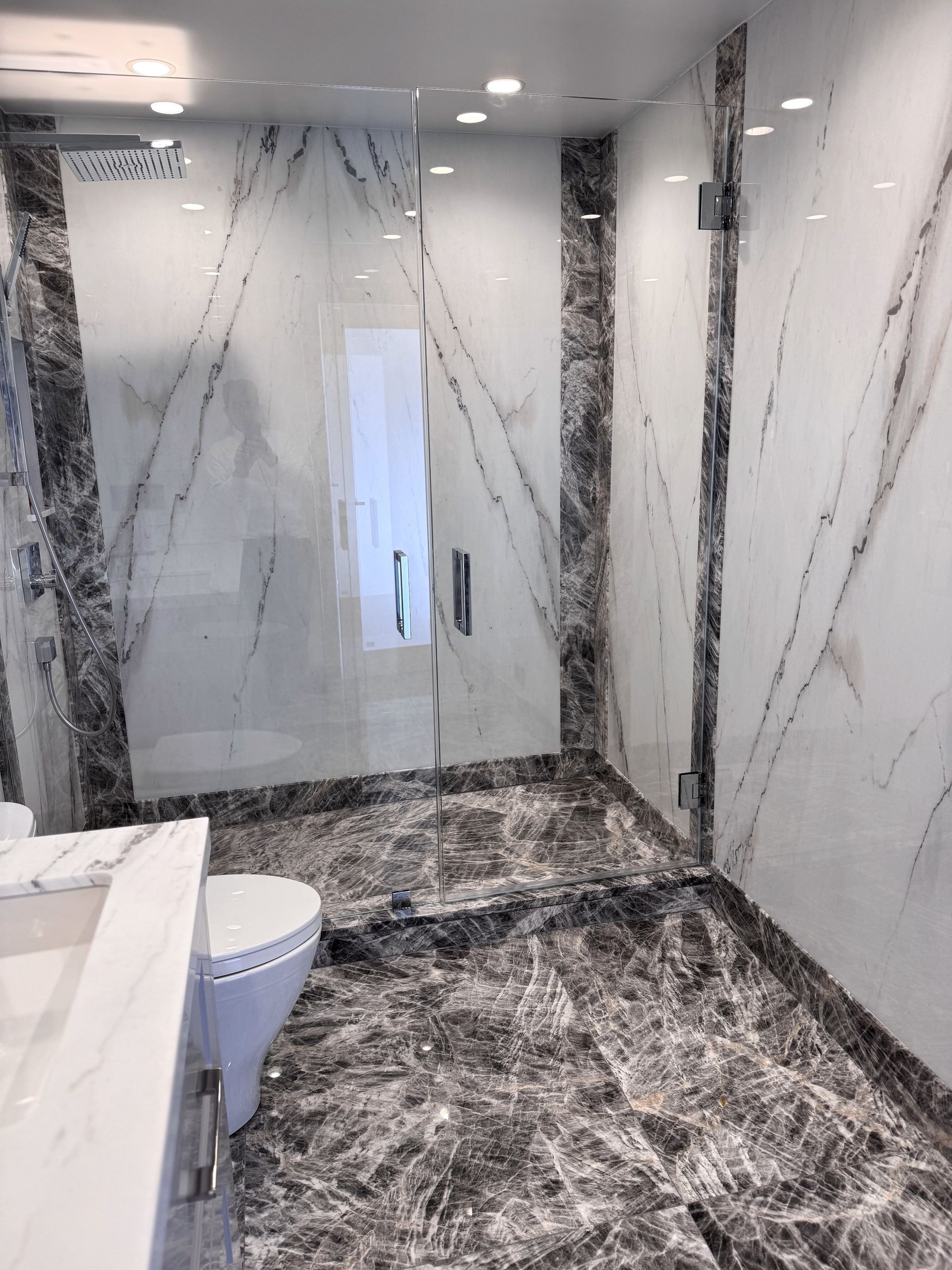 A bathroom with a toilet , sink , shower and marble floor.