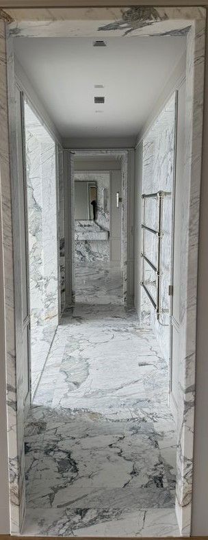 A long hallway with a marble floor and a door in the middle of it.