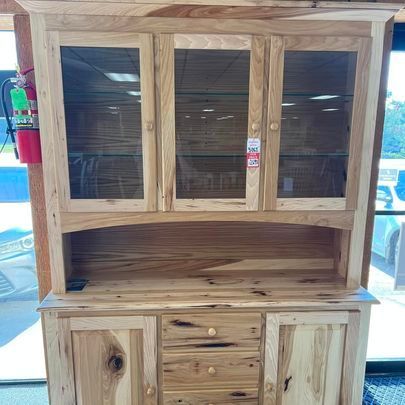 A wooden hutch with glass doors and drawers is sitting in a room.