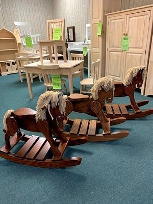 A room filled with wooden rocking horses and chairs.