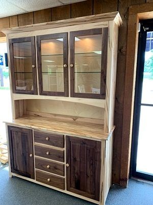A wooden cabinet with glass doors and drawers is sitting in a room next to a window.