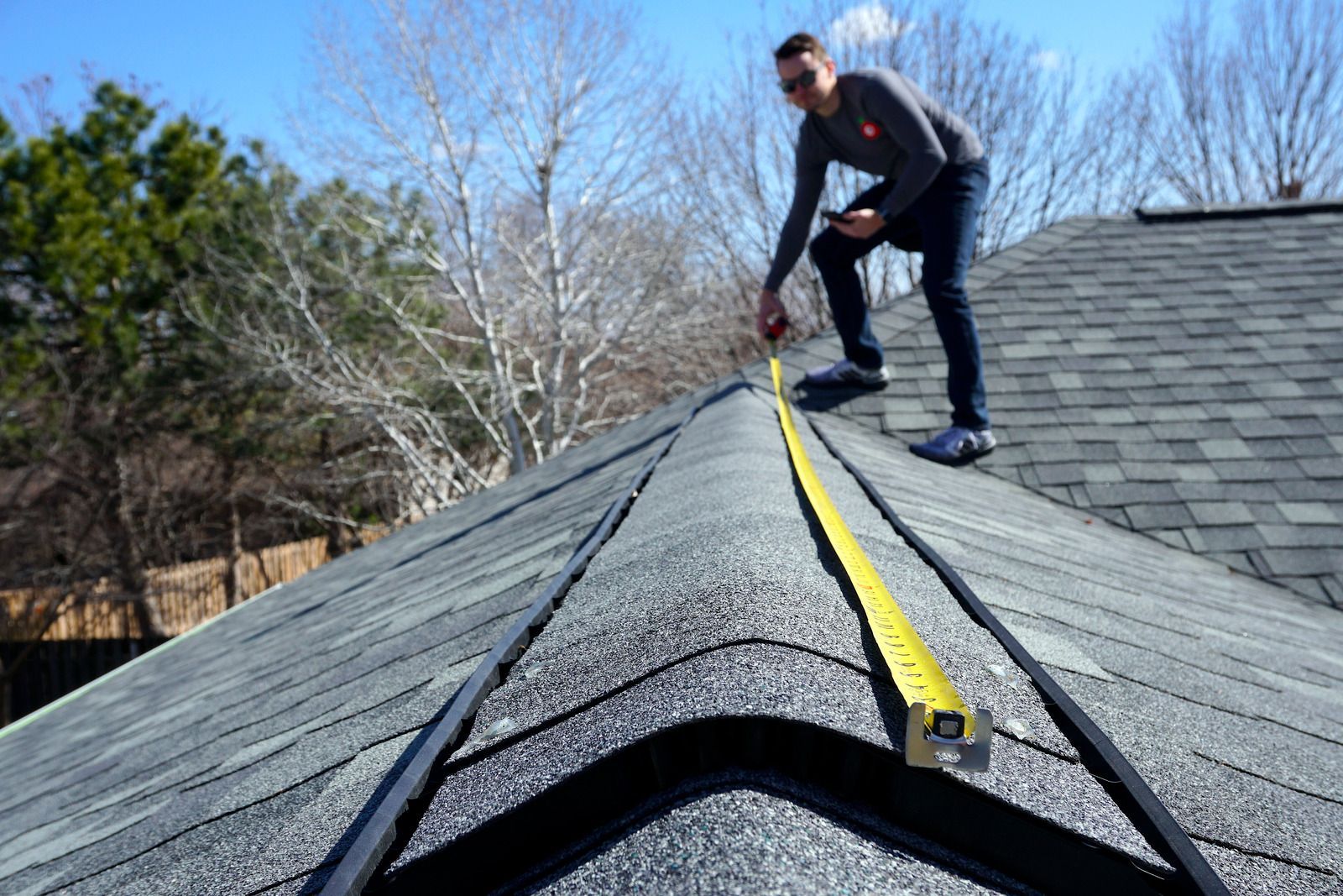 Person in safety gear inspects rooftop solar panels with mountains in the background.