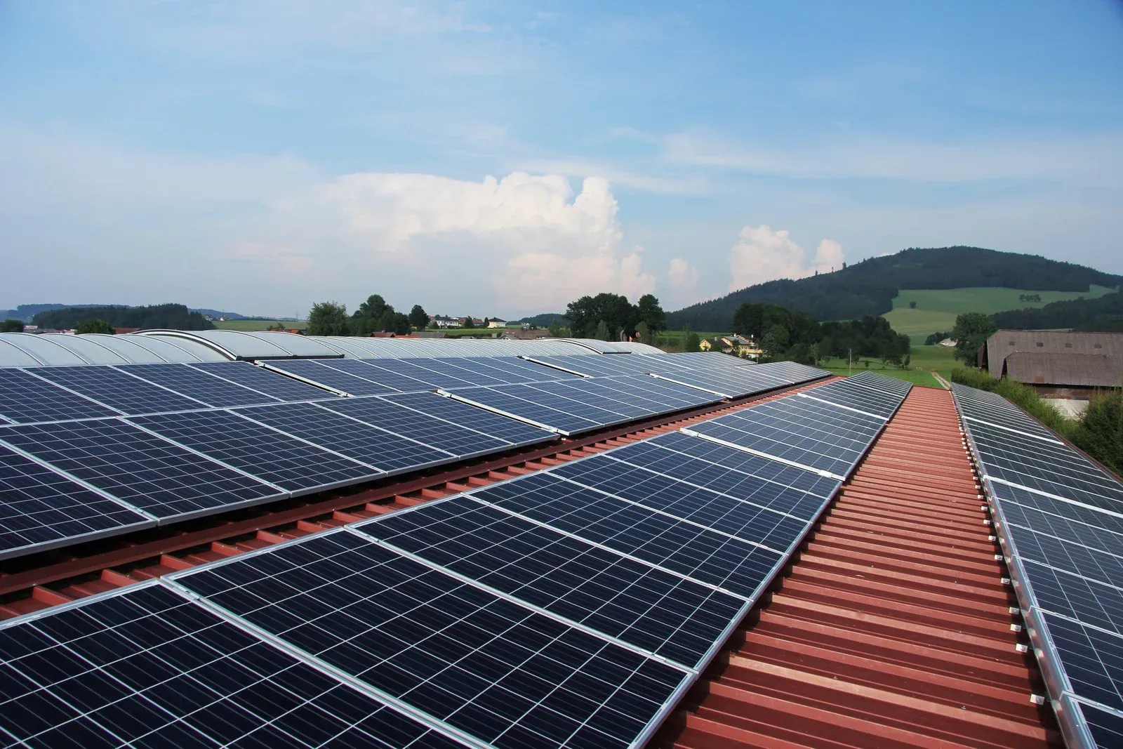 Solar panels installed on a red-tiled roof, with a green landscape and blue sky background.