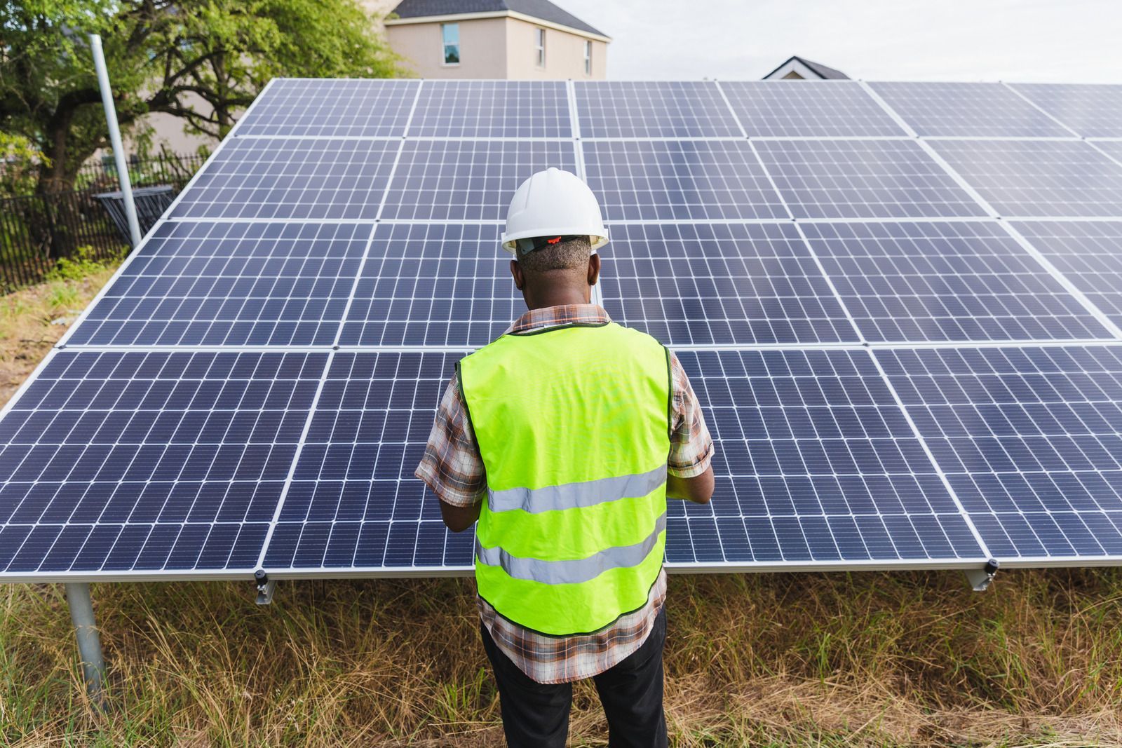 A man wearing a hard hat and safety vest is standing in front of a solar panel.