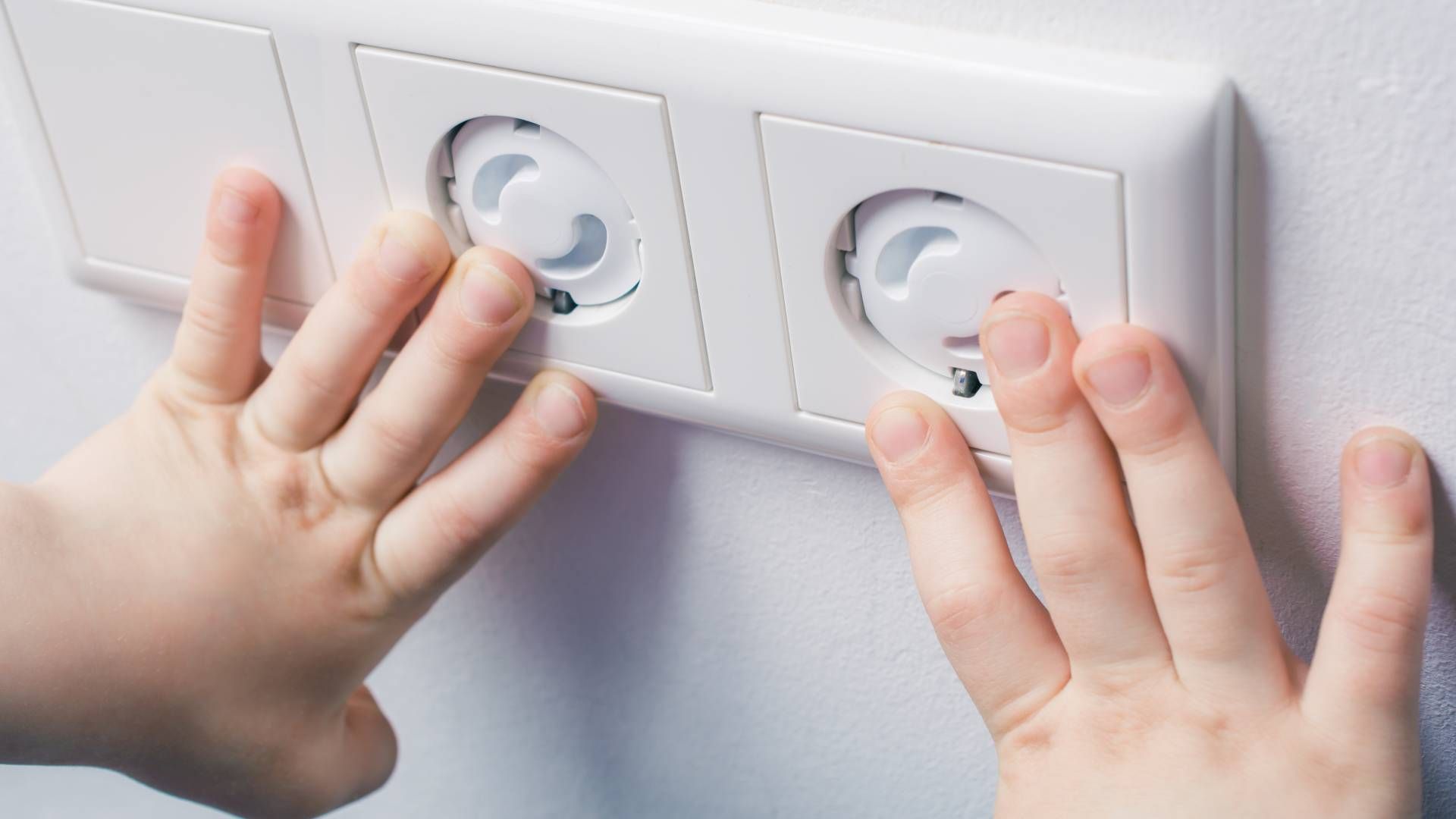 A pair of child's hands touching child-safe outlets in a safe and comfortable childcare facility at 