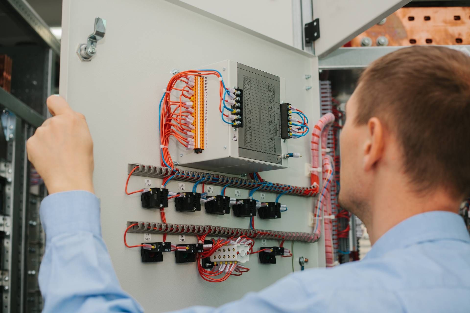 A low-voltage electrician in a blue shirt is checking in on low-voltage equipment in a cabinet