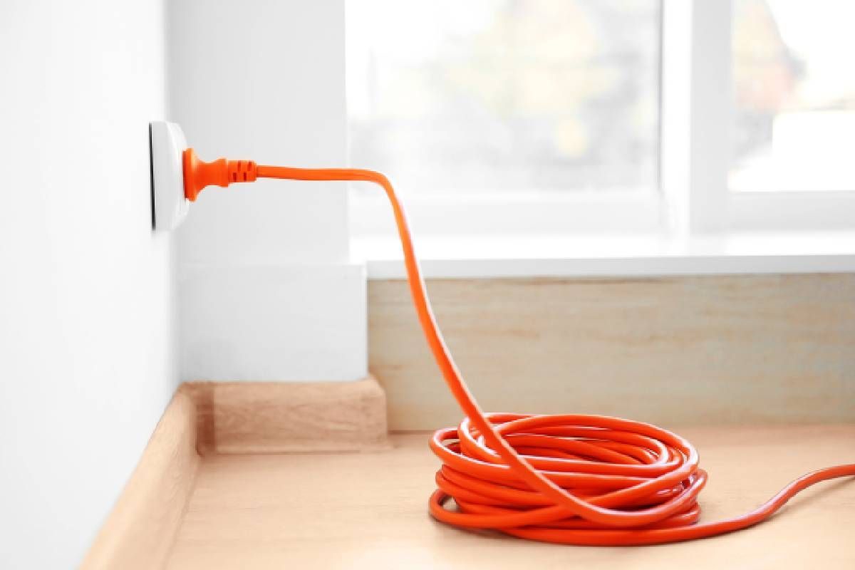 A coiled extension cord plugged into a wall outlet next to a window near Lexington, KY