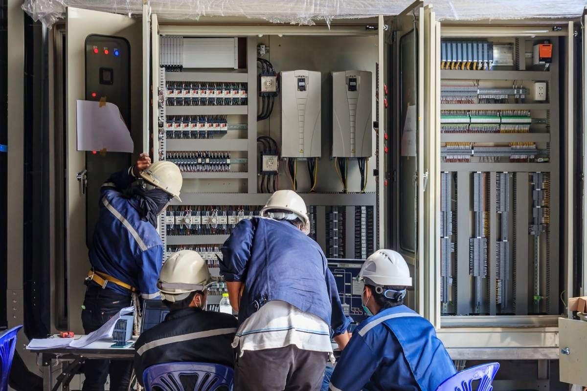 Four industrial electricians in white safety hats and blue jackets working on equipment at Walker Electric near Lexington, KY