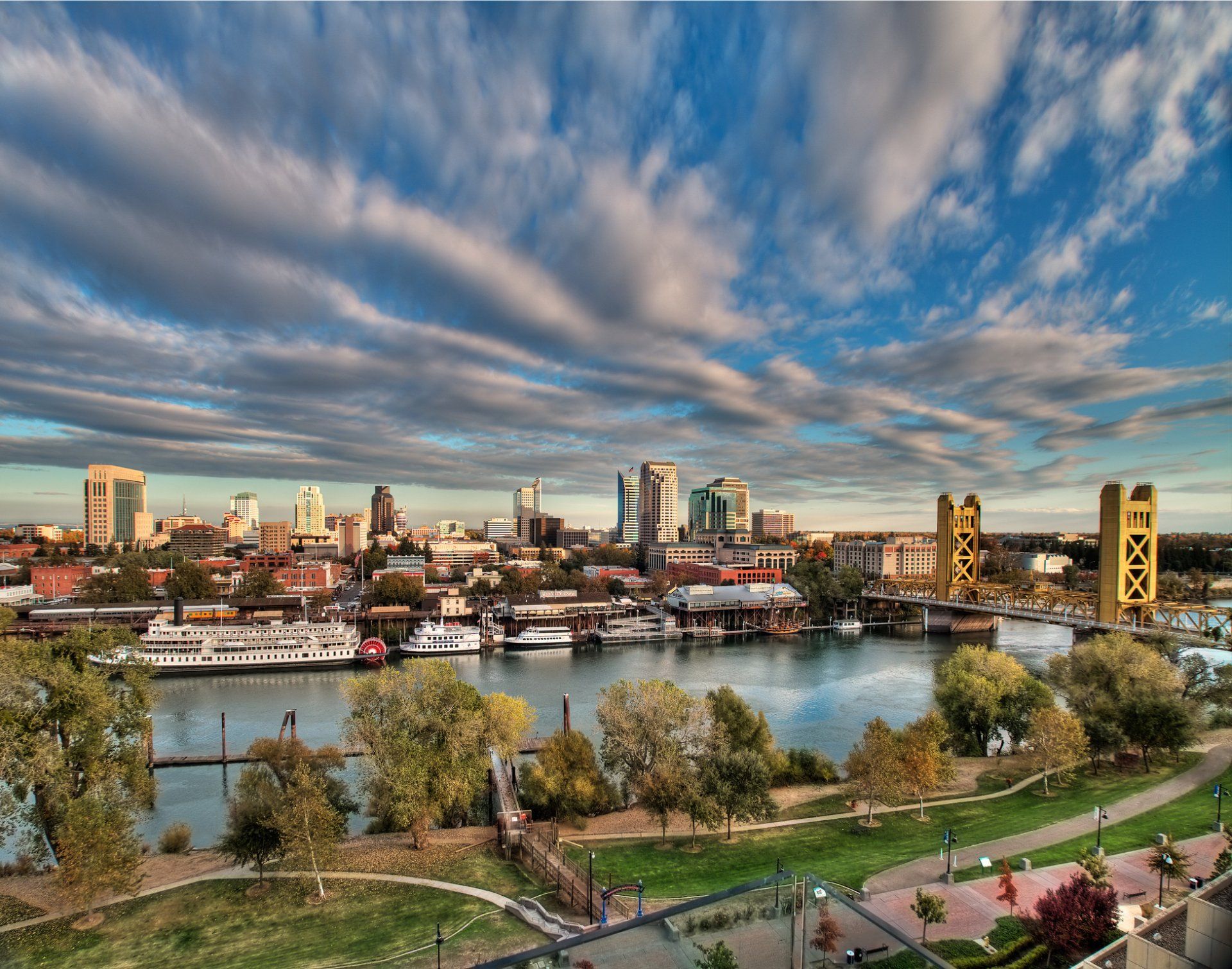 Sacramento, CA skyline overlooking the Sacramento River, under a cloudy blue sky.