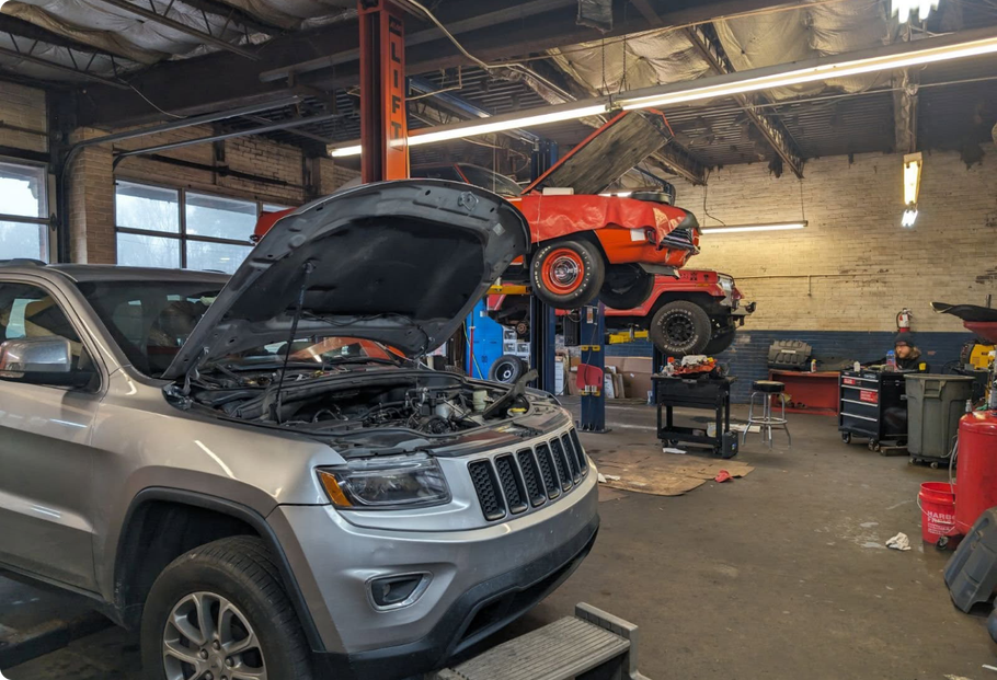 A jeep is sitting on a lift in a garage with its hood open.