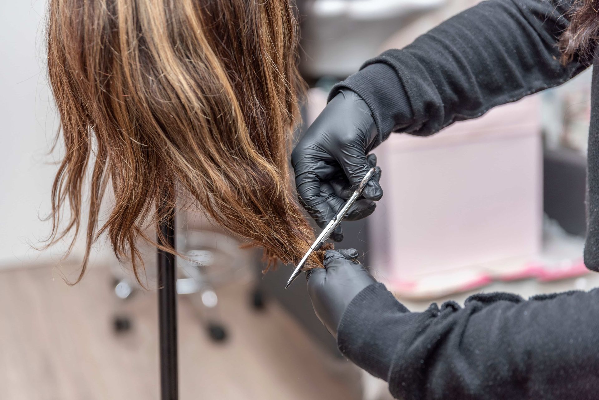 Gloved stylist cutting long brown hair with scissors in a salon