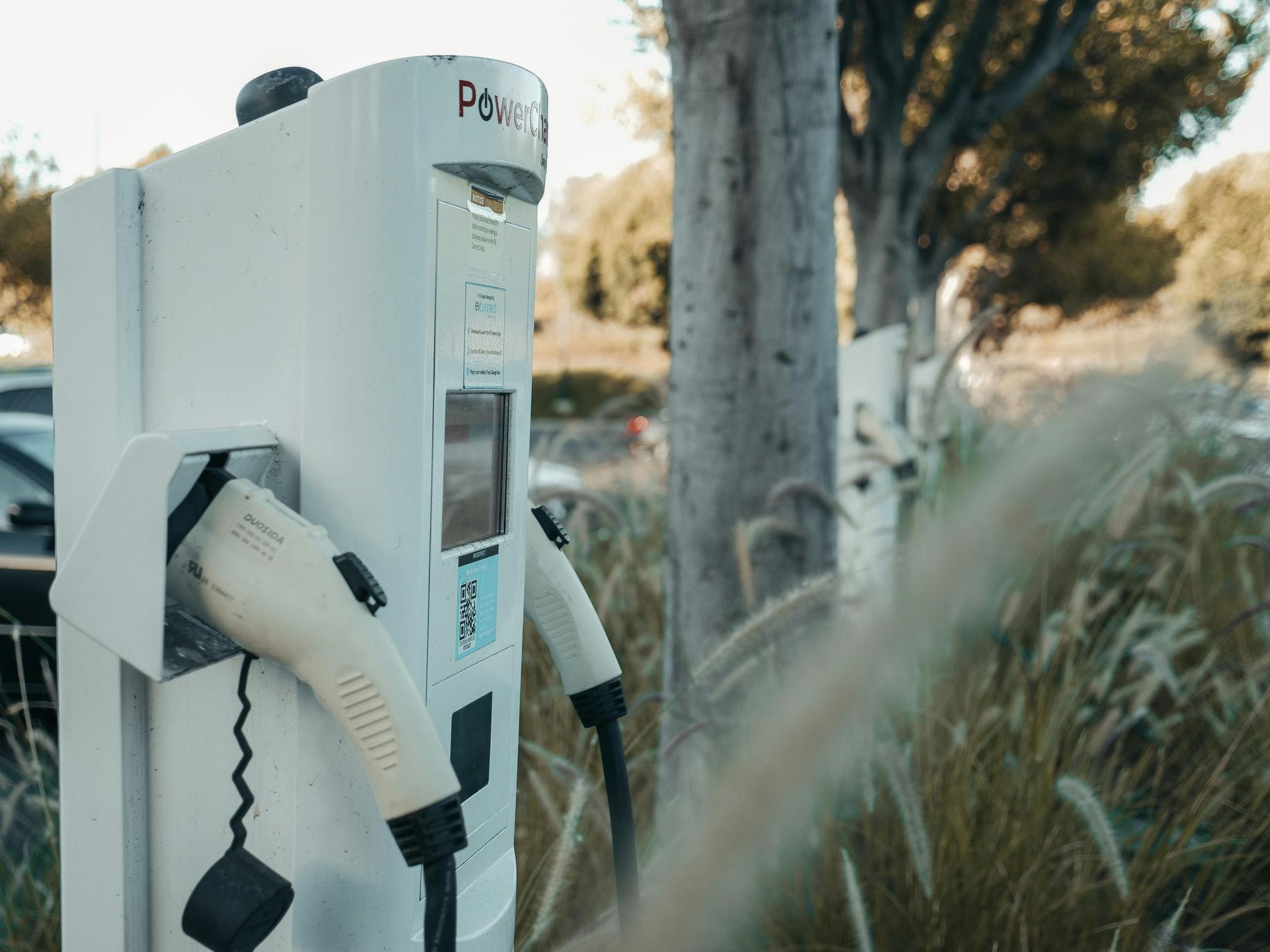 Electric vehicle charging station with white cables, outdoors.