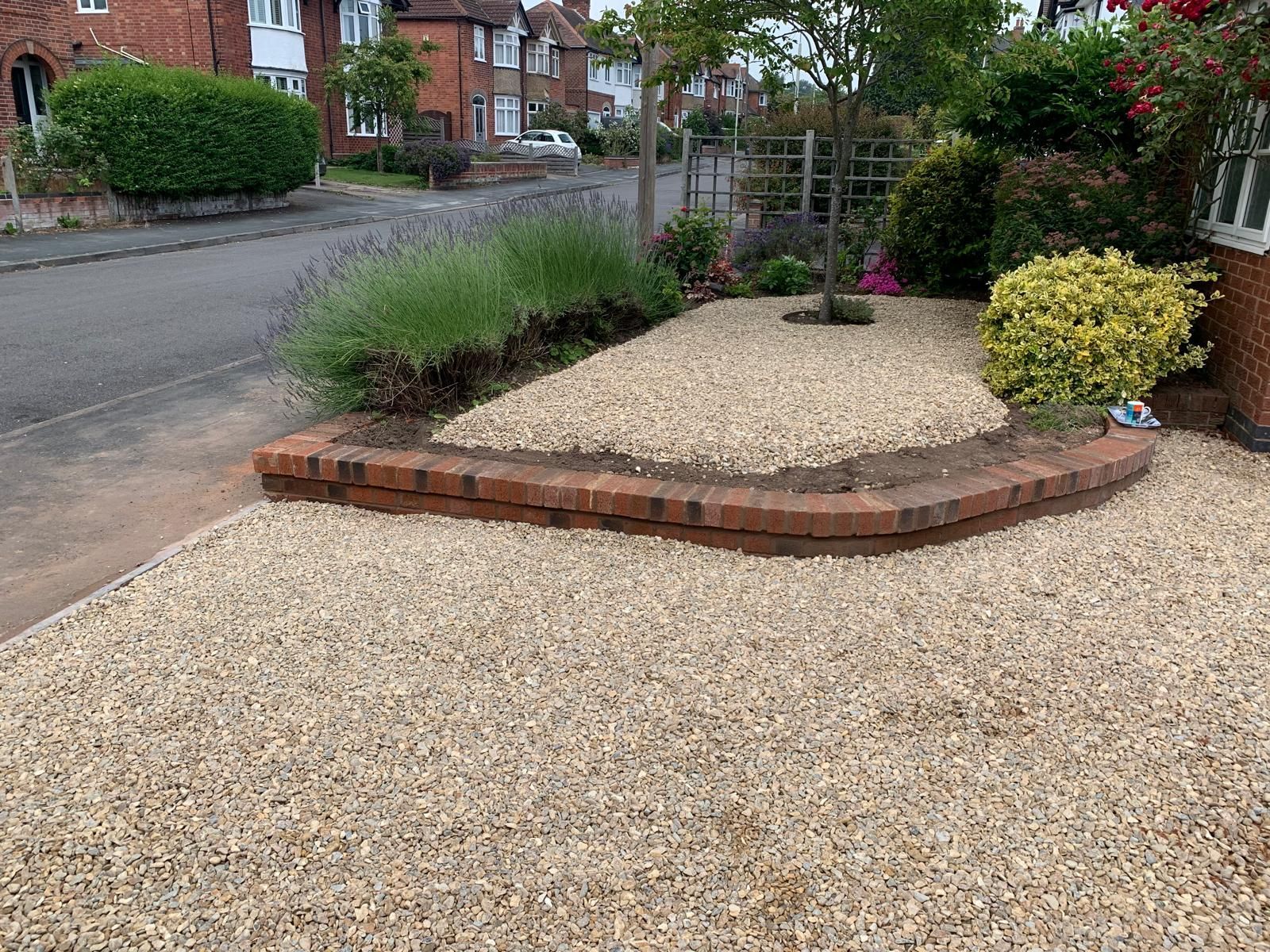 A gravel driveway with a brick border and a tree in the middle of it.