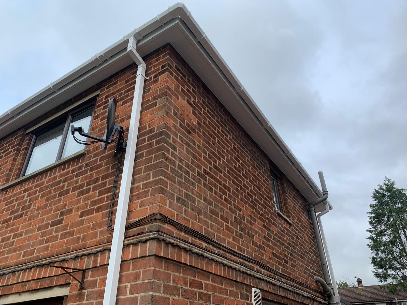 A red brick house with a white gutter and satellite dish on the side.