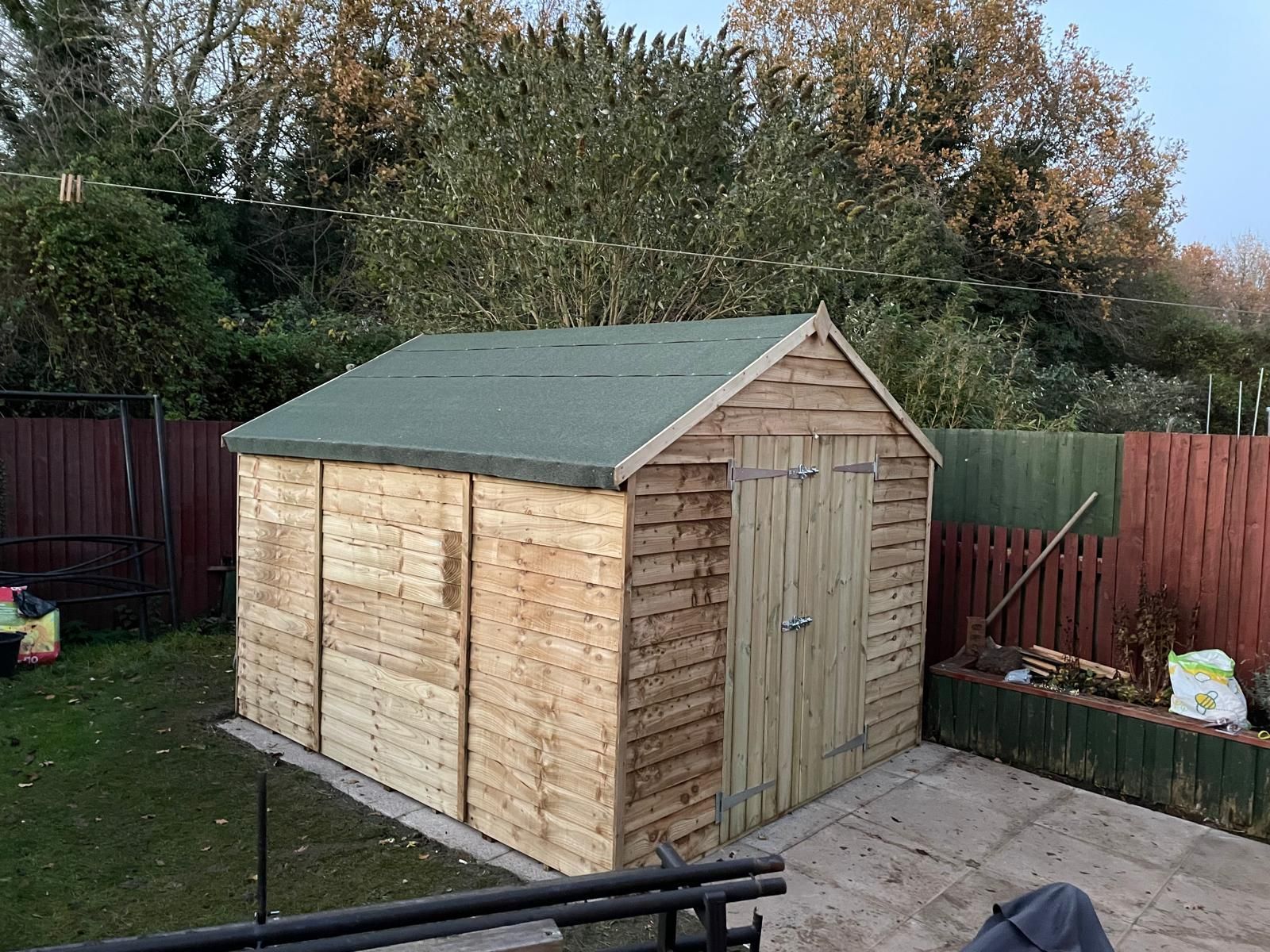 A wooden shed with a green roof is in a backyard.