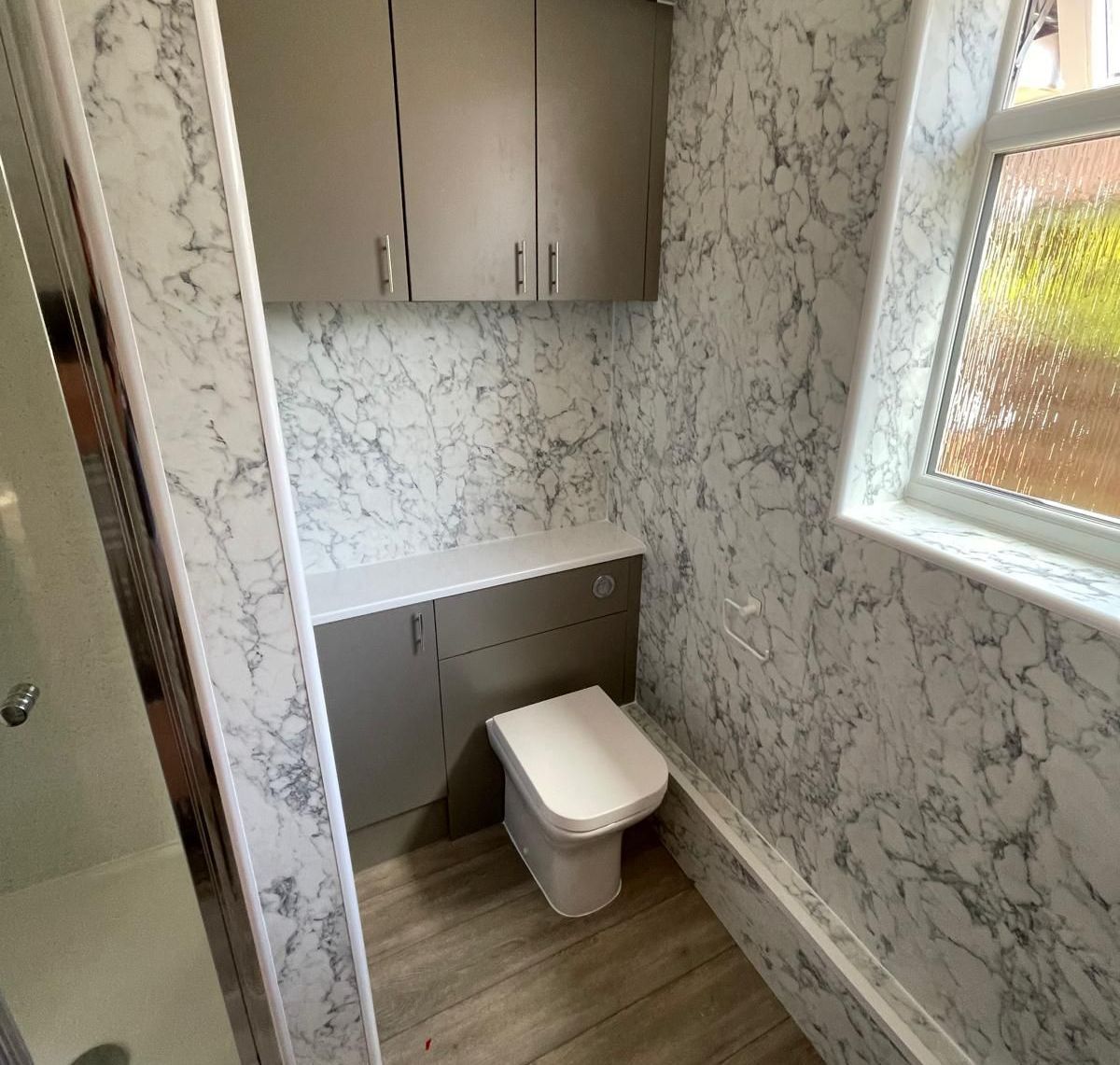 A bathroom with a toilet , cabinets , and a window.
