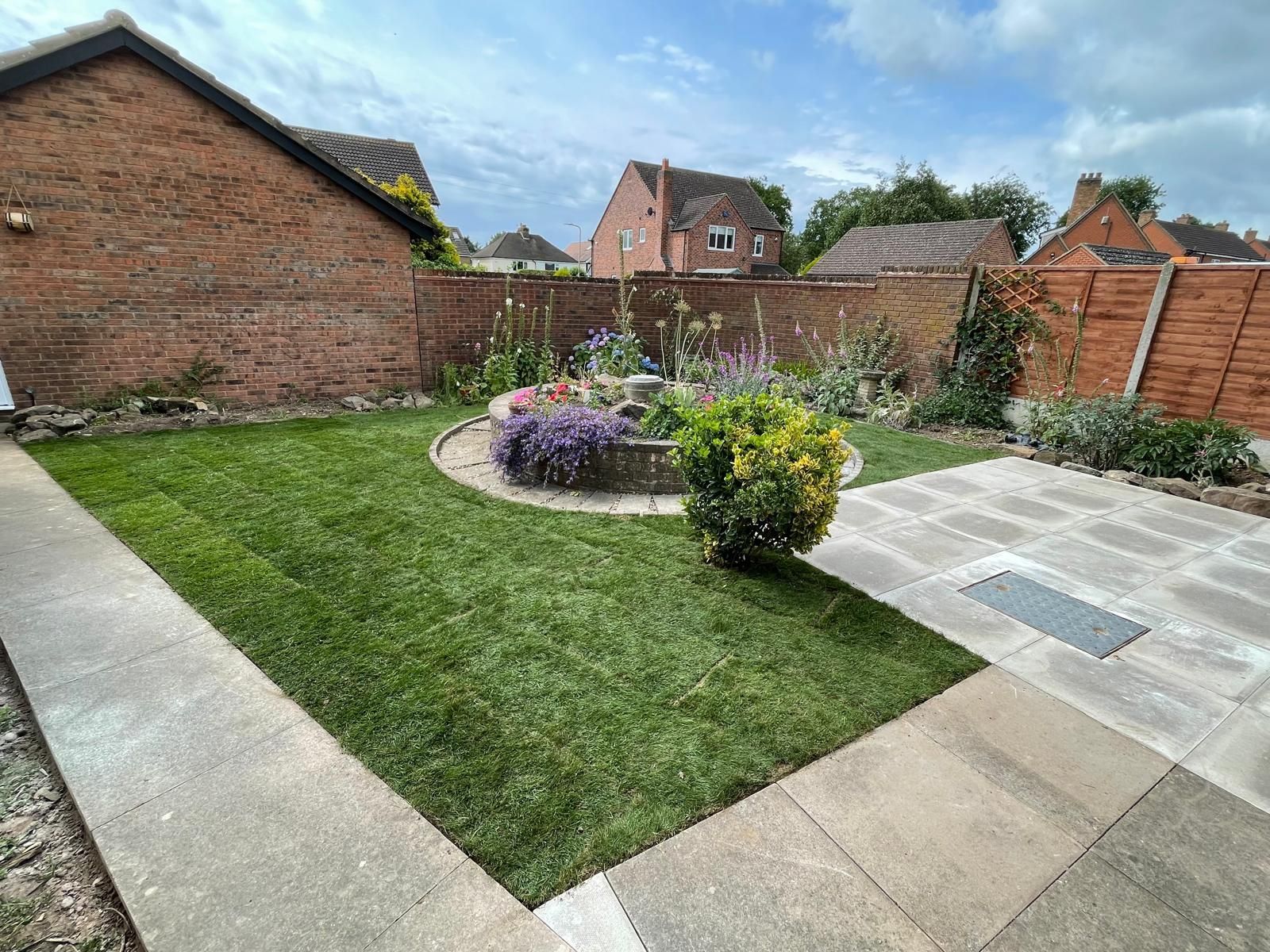 A lush green backyard with a brick fence and a patio.