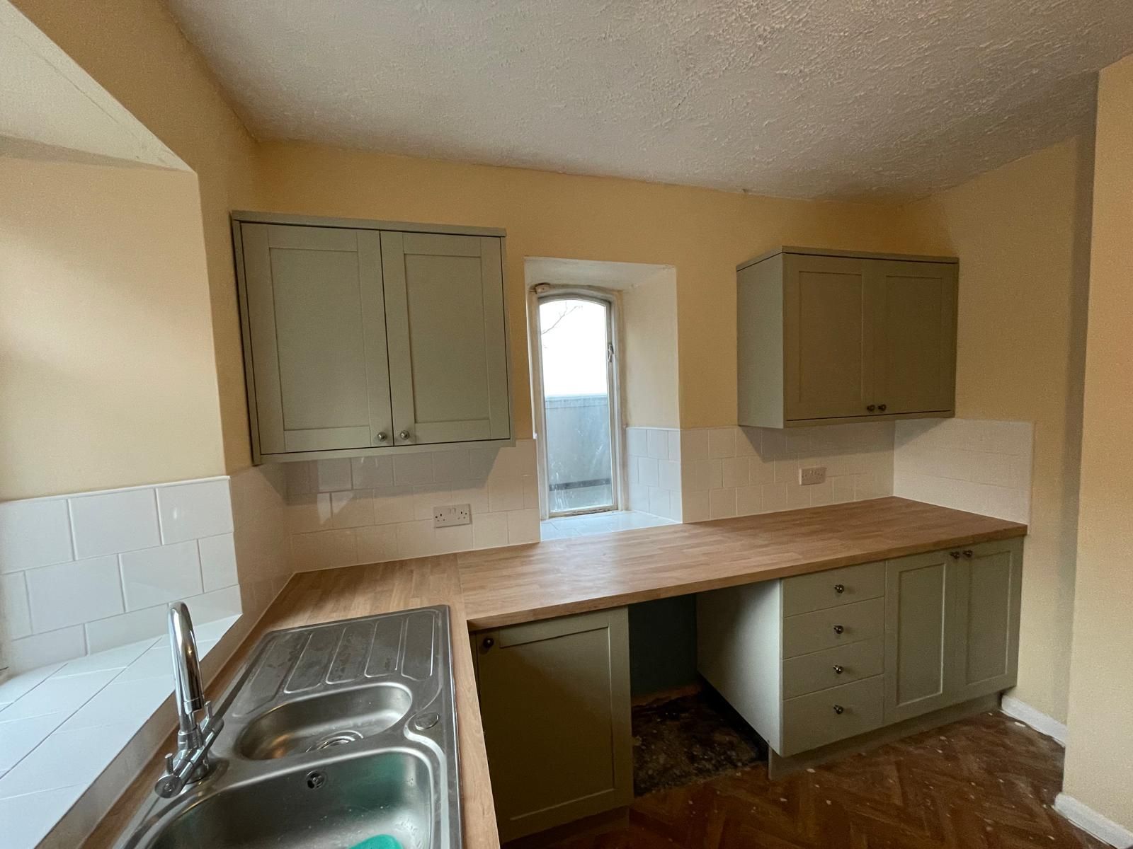 An empty kitchen with a sink , cabinets , and a window.