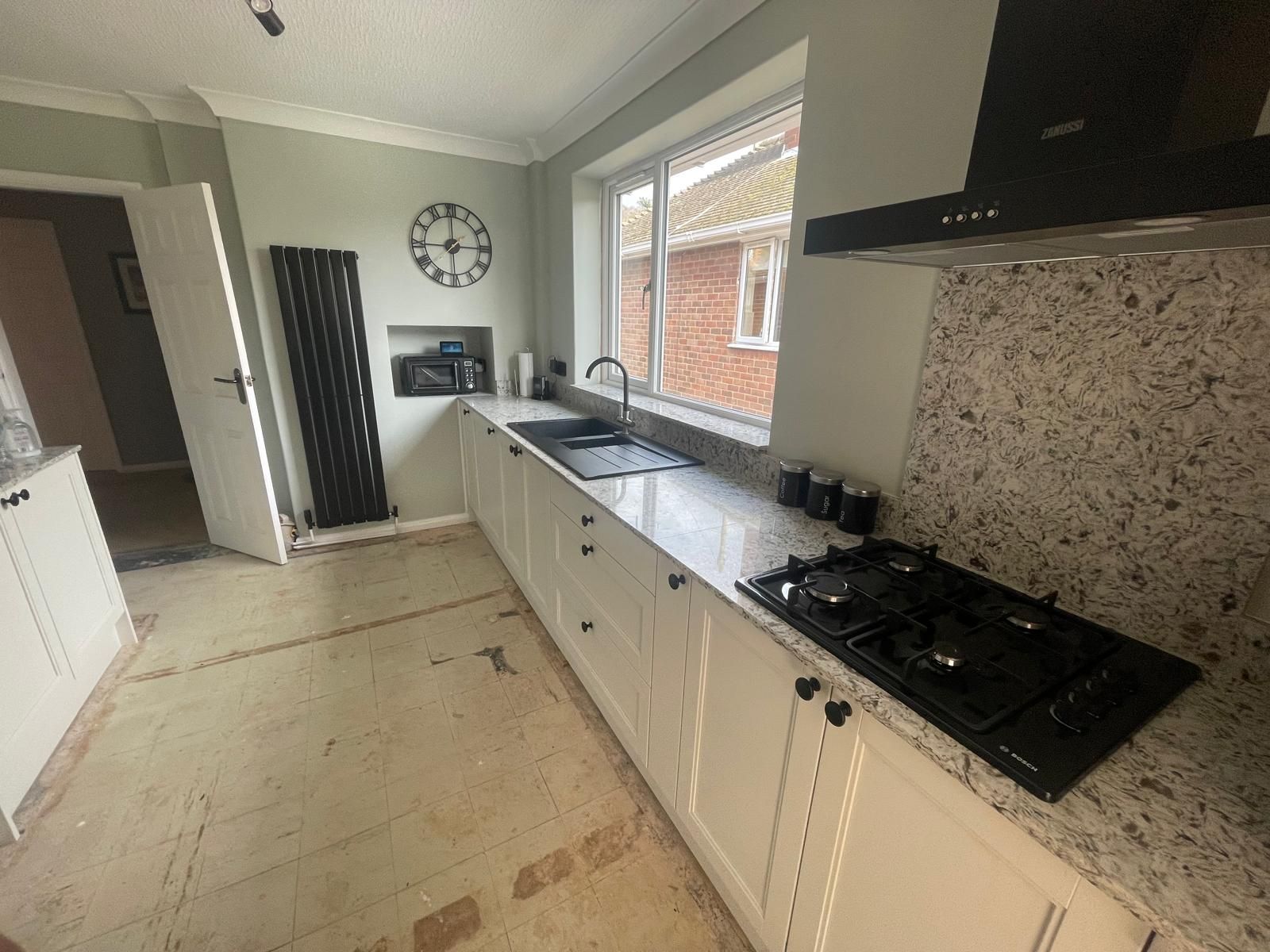 A kitchen with white cabinets , a stove , a sink and a clock on the wall.