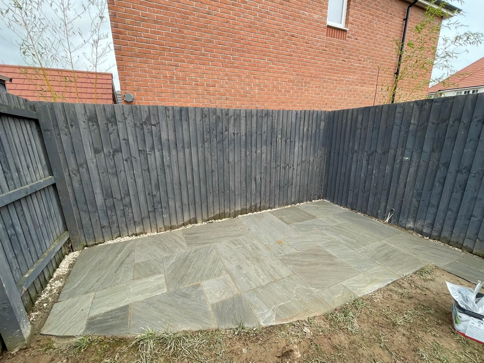 A corner of a backyard with a wooden fence and a concrete patio.