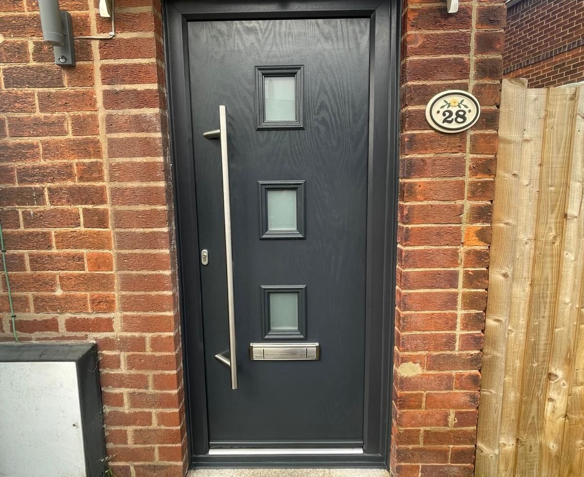 A black door is on a brick wall next to a wooden fence.