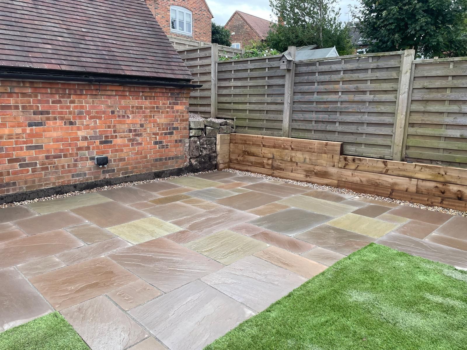 A patio with a wooden fence and a brick wall in a backyard.