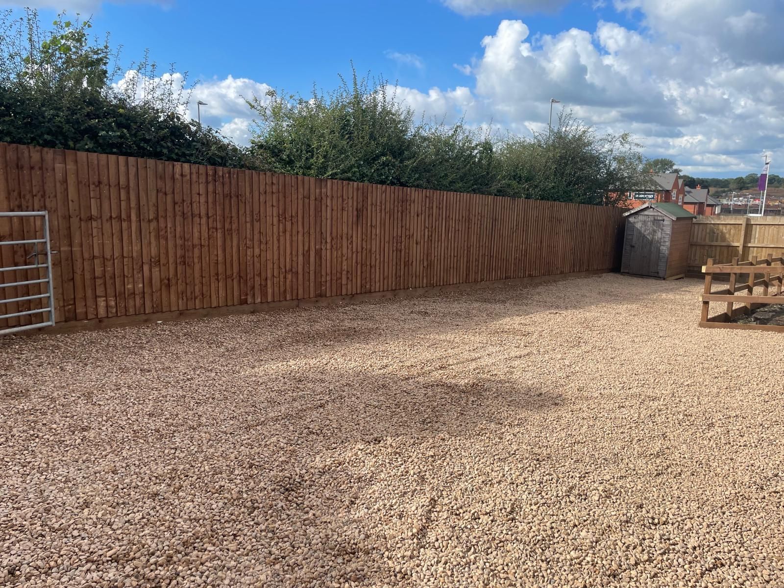 A wooden fence surrounds a gravel area in a backyard.