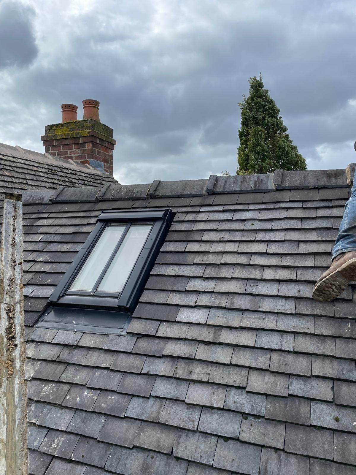 A person is sitting on top of a roof with a skylight.