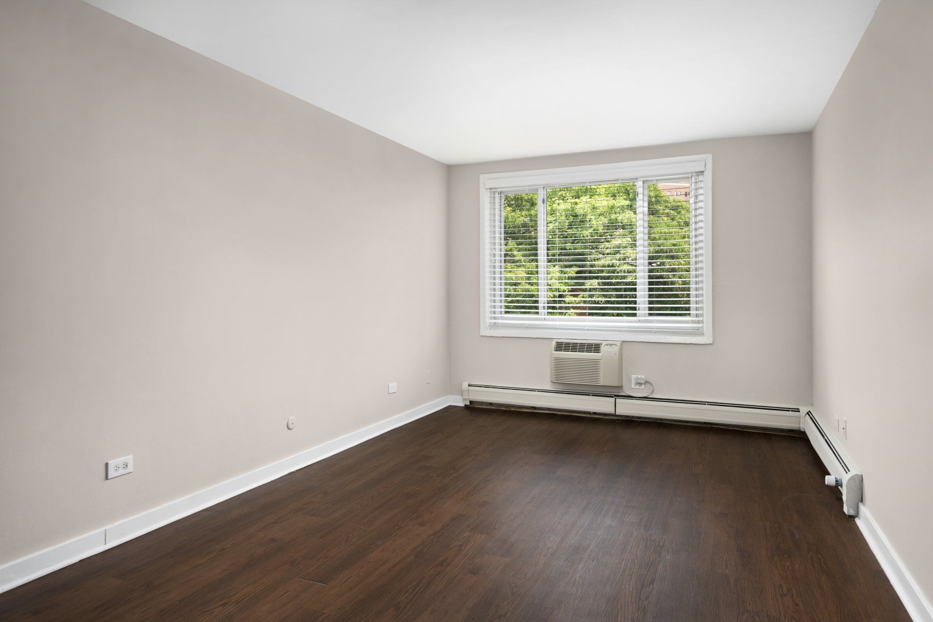 An empty room with hardwood floors, AC, and a window at Reside 707.