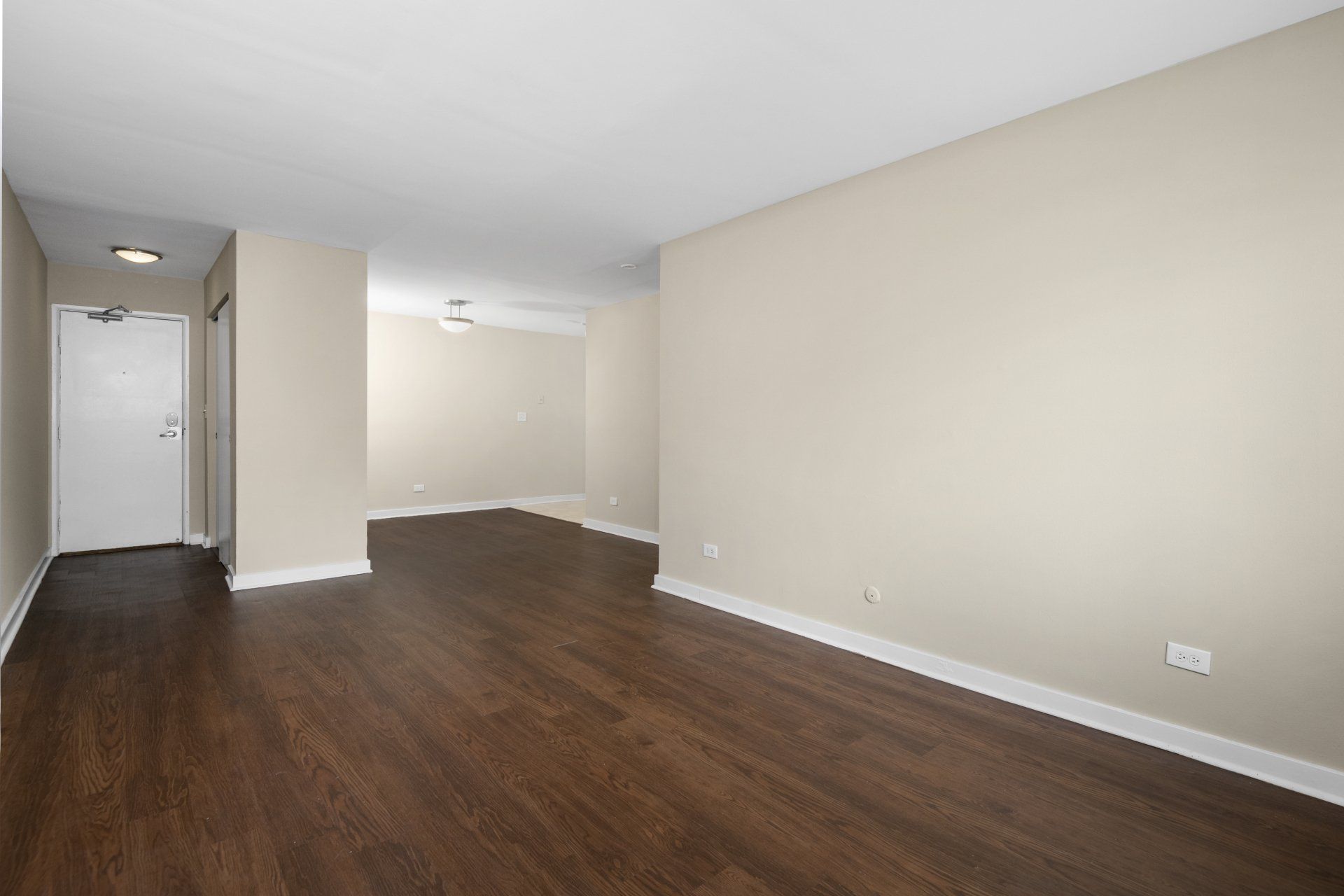 An empty living room with hardwood floors and beige walls at Reside 707.
