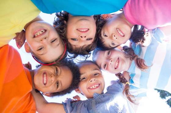 Eine Gruppe lächelnder Kinder in bunten Hemden blickt aus einem niedrigen Winkel nach unten.