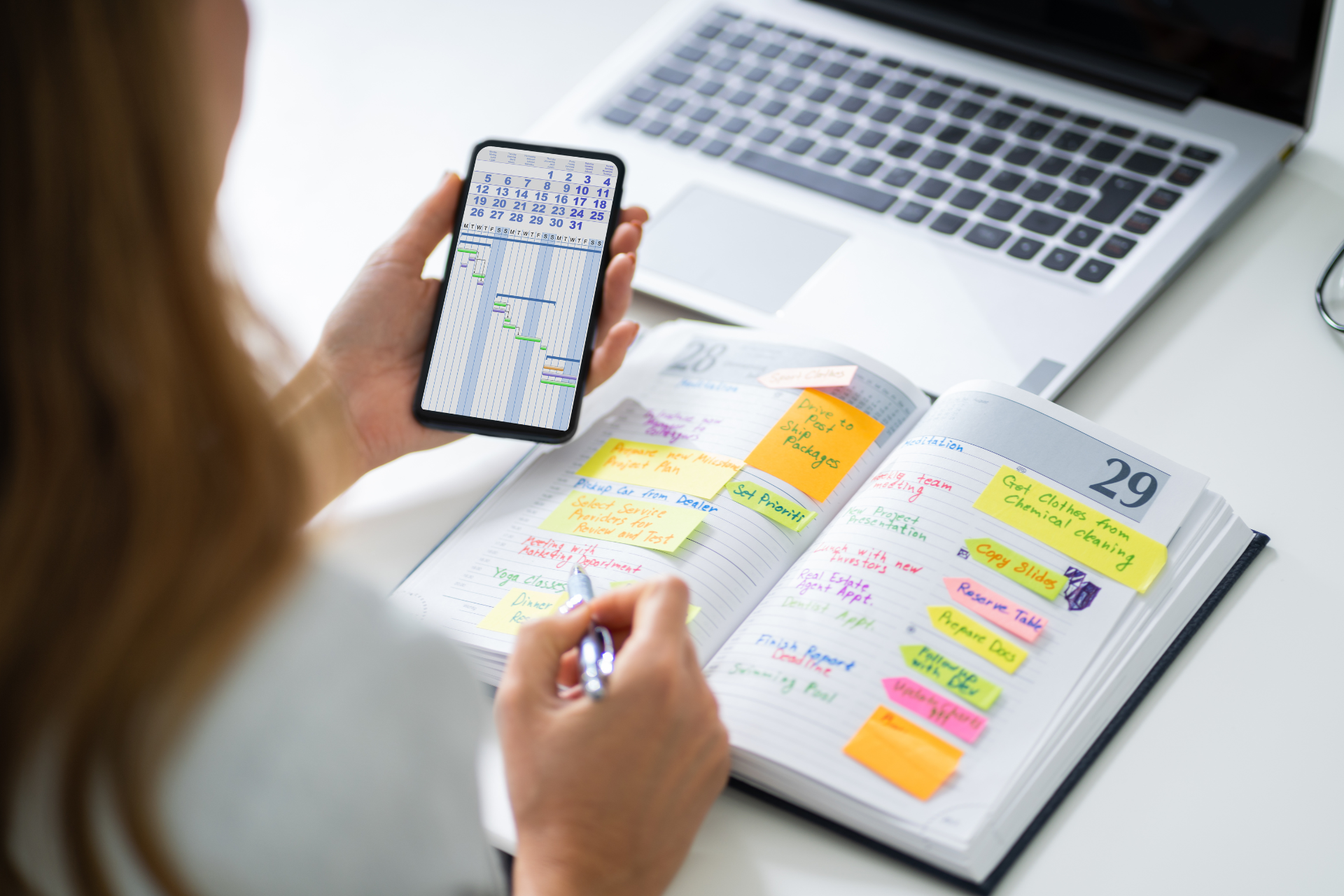 Frau vergleicht einen Telefonkalender mit einem handgeschriebenen Planer, im Hintergrund ein Laptop.