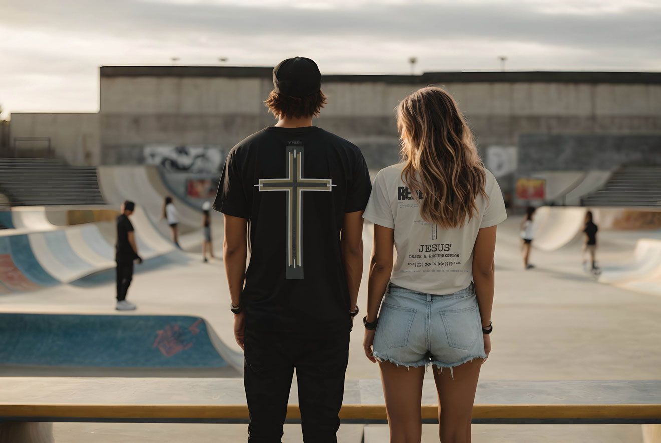 Two people at a skate park, facing away. Man wears a black shirt with a cross. Woman wears a white shirt and jean shorts.