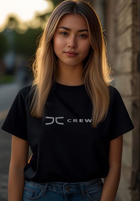 Young woman with blonde hair wearing a black t-shirt with white logo, standing near a brick wall.