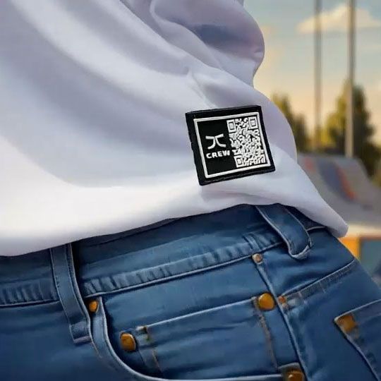 Person wearing a white shirt and jeans; a patch with a logo and QR code is on the shirt.