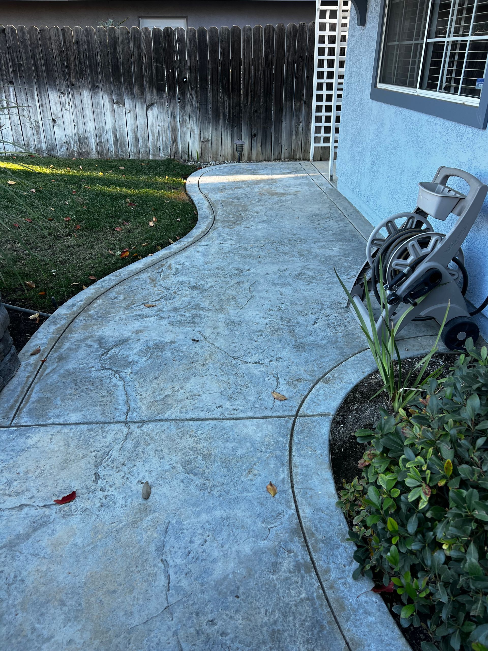A concrete walkway leading to a house with a hose on the side of it.