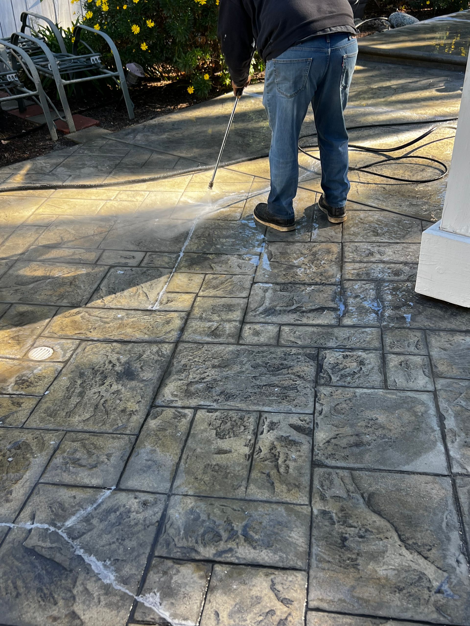 A man is cleaning a concrete patio with a hose.