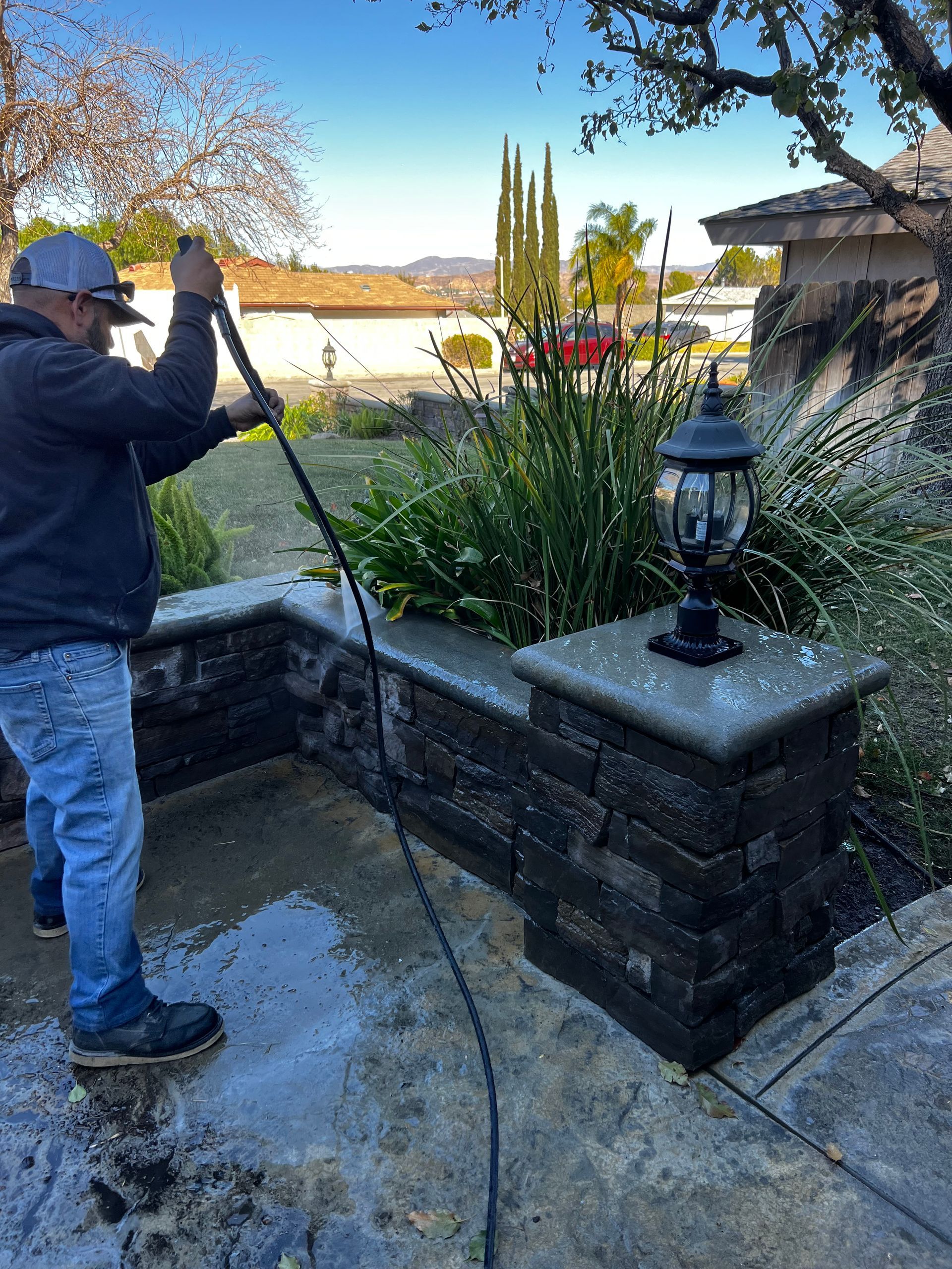 A man is cleaning a sidewalk with a high pressure washer.